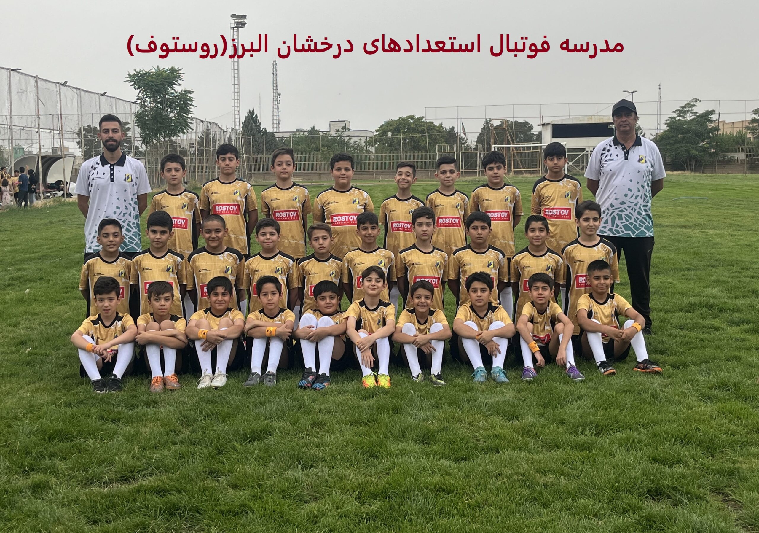 تصویر گروهی از یک تیم فوتبال کودکان با لباس‌های زرد و مشکی حاوی لوگوی "Rostov"، همراه با مربیان در زمین چمن